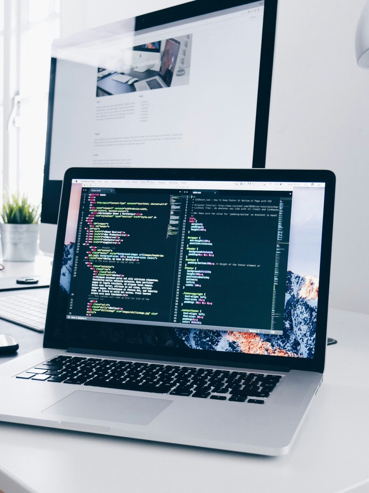 A MacBook with lines of code on its screen on a busy desk
