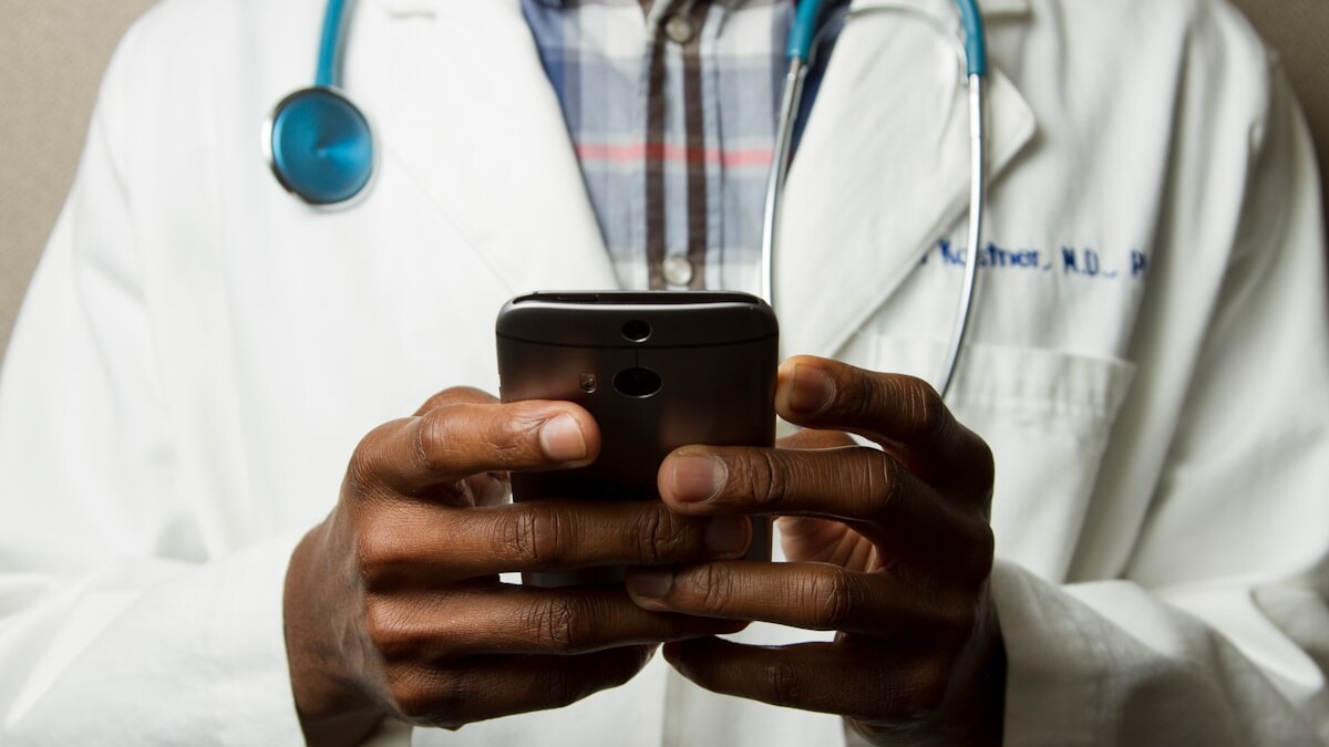 person wearing lavatory gown with green stethoscope on neck using phone while standing