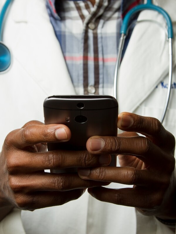 person wearing lavatory gown with green stethoscope on neck using phone while standing