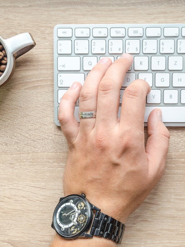 Person Using Silver Apple Magic Keyboard Beside of White Ceramic Mug With Coffee Beans