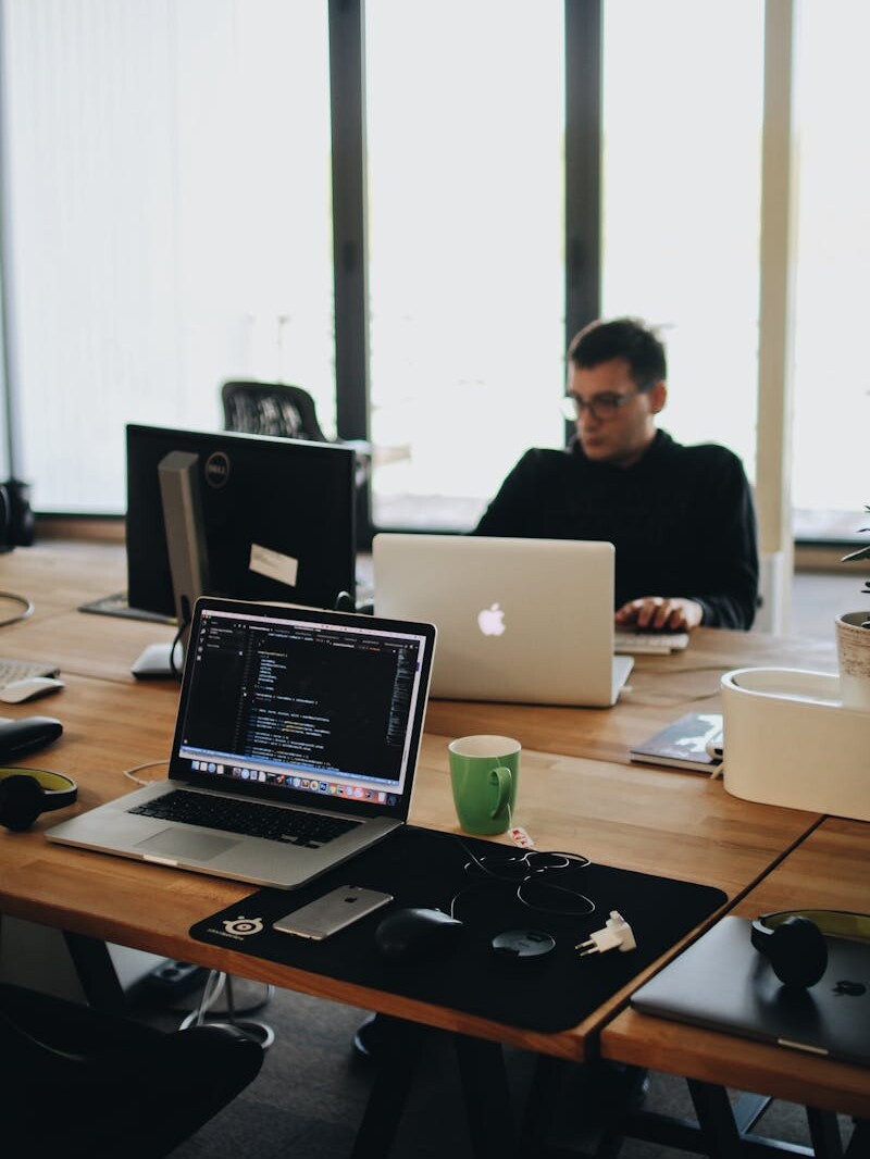 Man in Black Shirt Sits Behind Desk With Computers