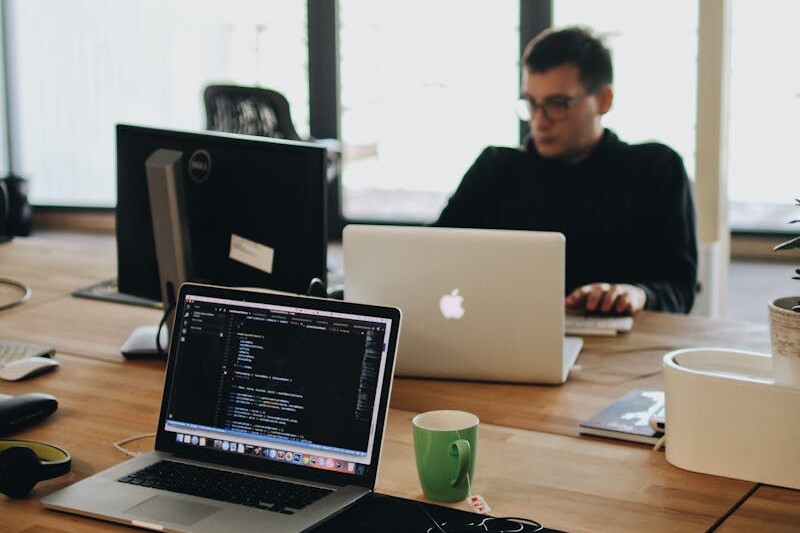 Man in Black Shirt Sits Behind Desk With Computers