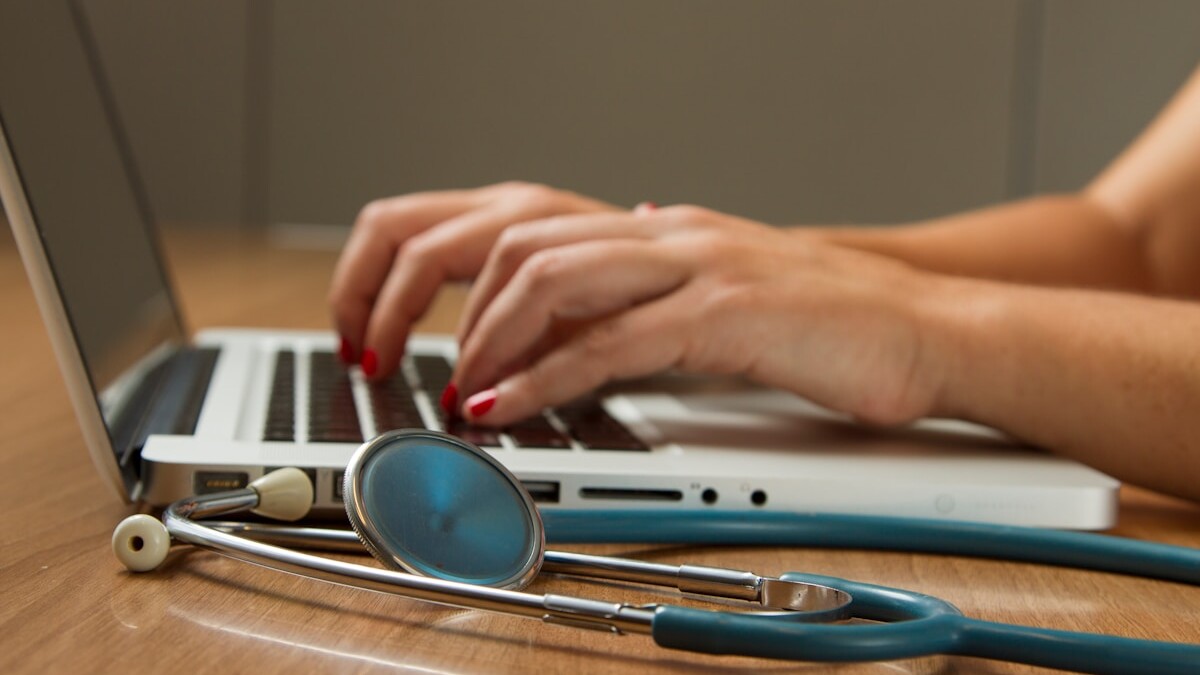 person sitting while using laptop computer and green stethoscope near