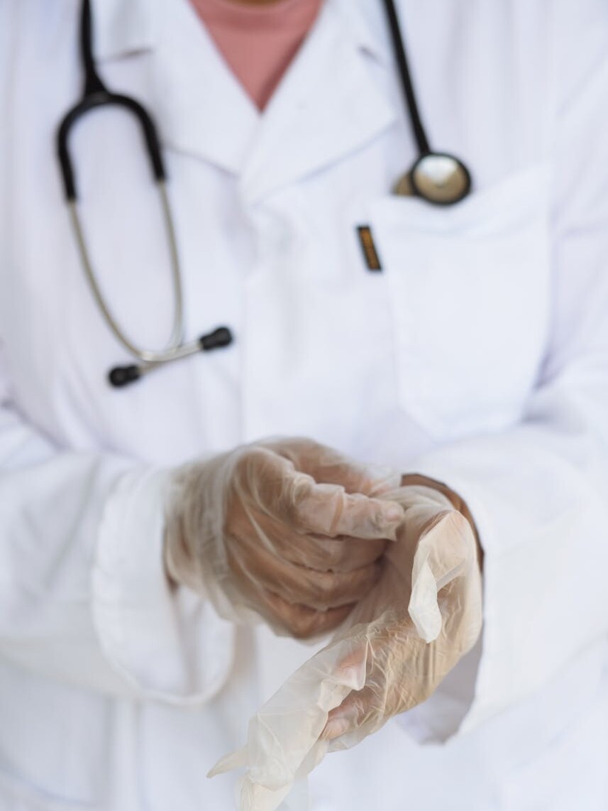 Faceless ethnic medical worker in lab coat and stethoscope taking of transparent gloves after approaching patients for examination in modern hospital