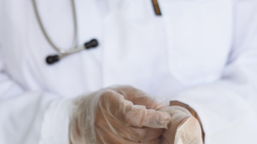 Faceless ethnic medical worker in lab coat and stethoscope taking of transparent gloves after approaching patients for examination in modern hospital