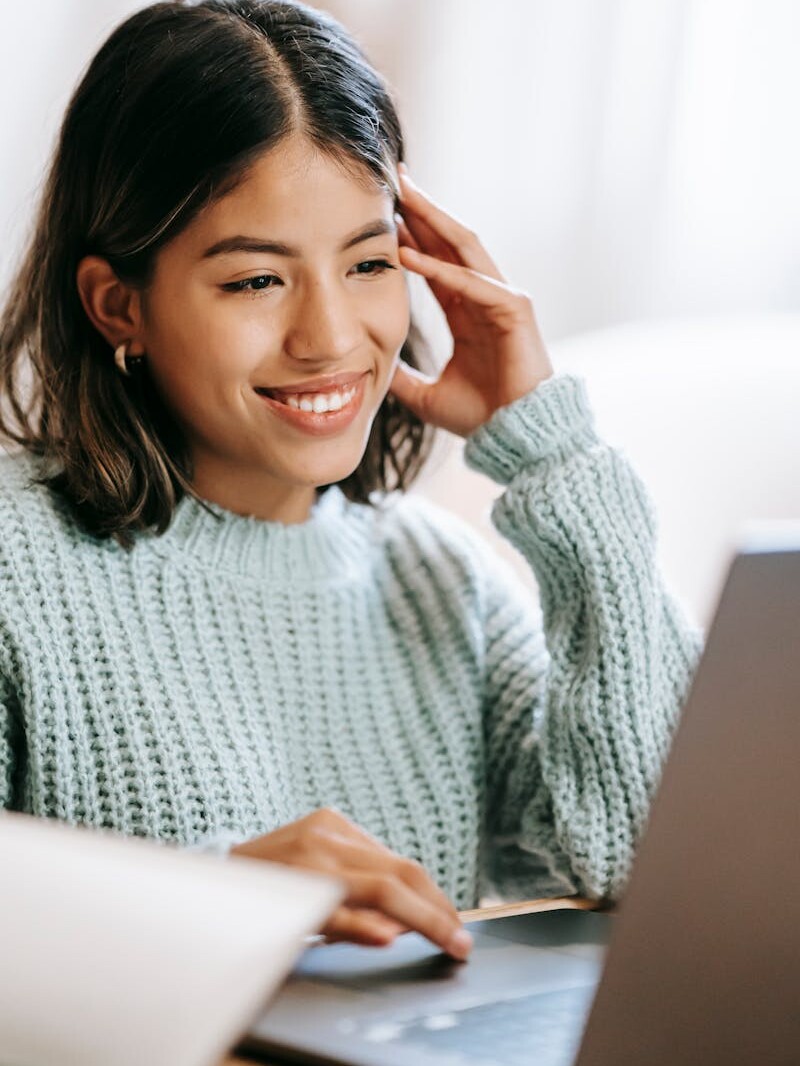 Hispanic woman working remotely on laptop near notepad in apartment