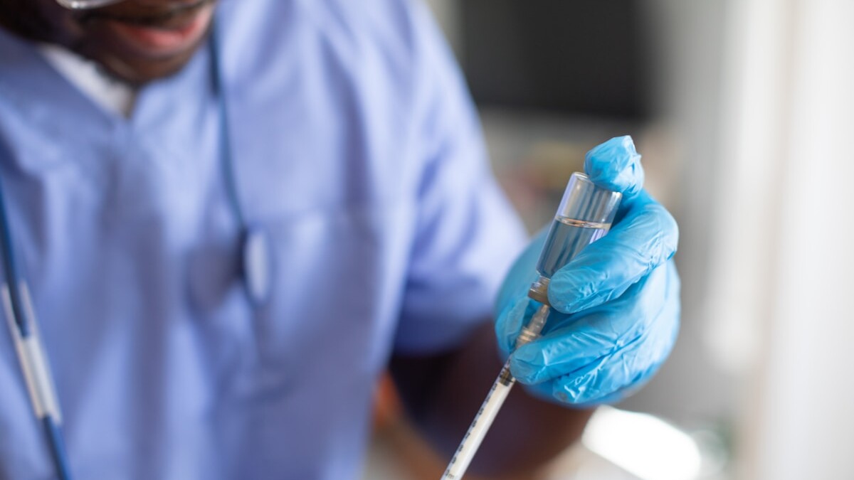 a person wearing a lab coat and gloves holding a syringe