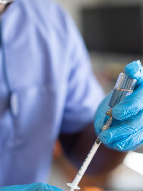 a person wearing a lab coat and gloves holding a syringe