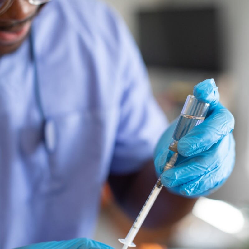 a person wearing a lab coat and gloves holding a syringe