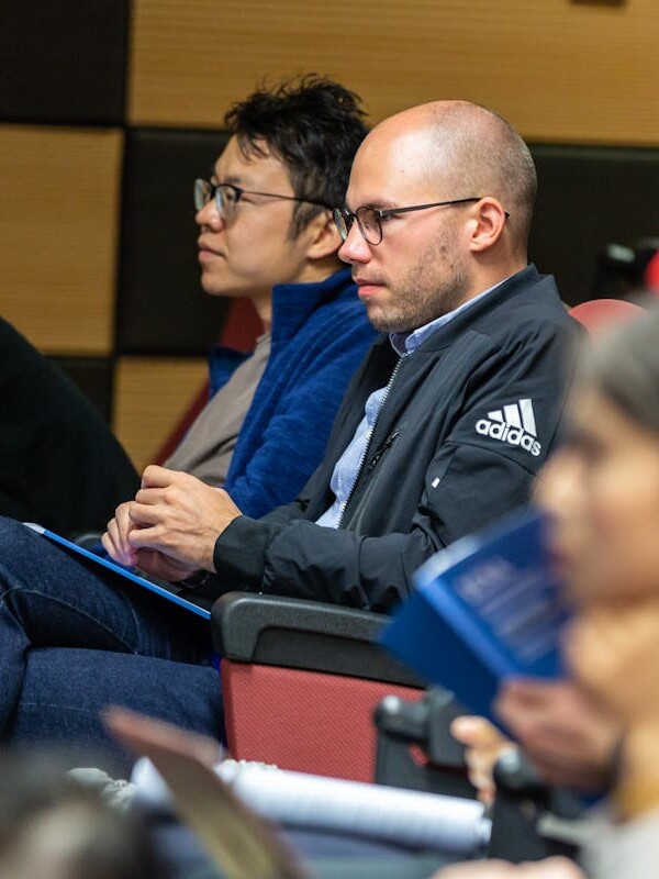 Man Wearing Black Adidas Jacket Sitting on Chair Near Another Man Wearing Blue Jacket