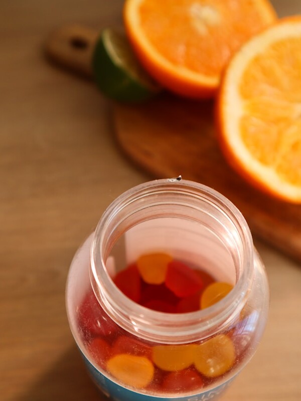 a jar filled with gummy bears next to sliced oranges