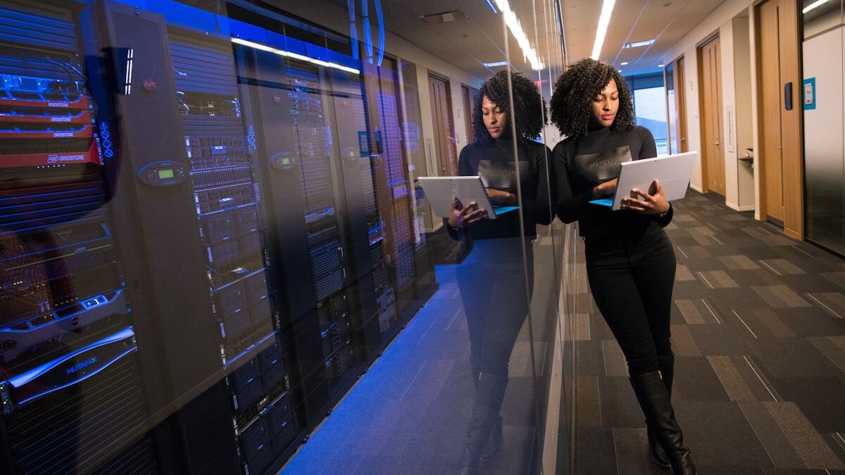 A woman using a laptop navigating a contemporary data center with mirrored servers.