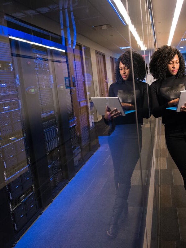 A woman using a laptop navigating a contemporary data center with mirrored servers.