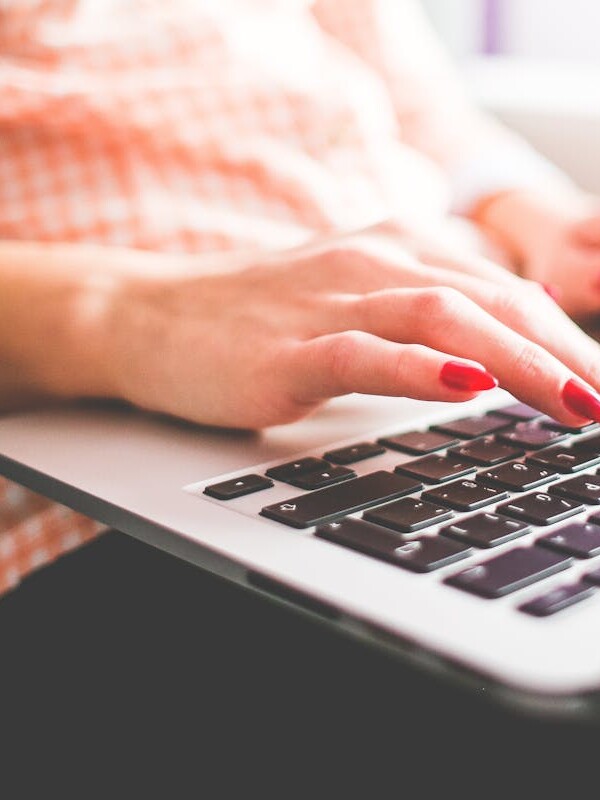 Close-up of a woman with red nails typing on a laptop indoors.