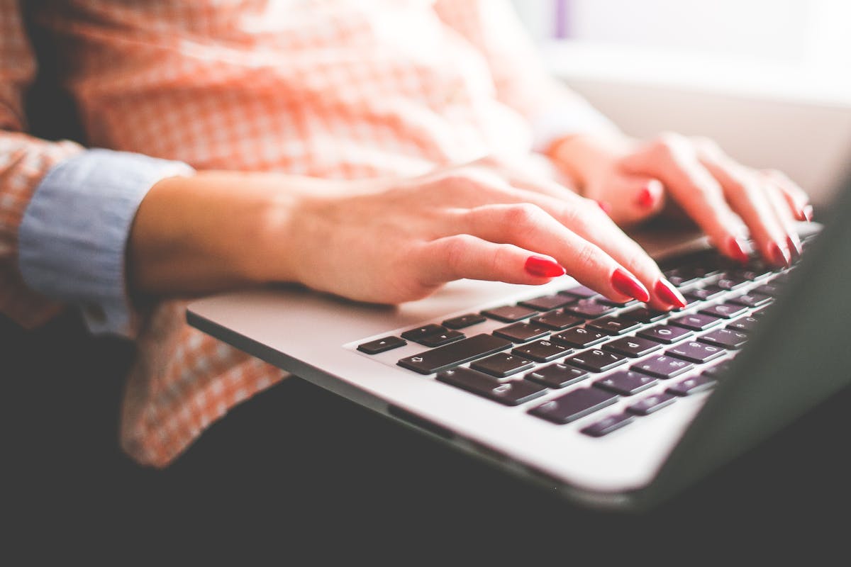 Close-up of a woman with red nails typing on a laptop indoors.