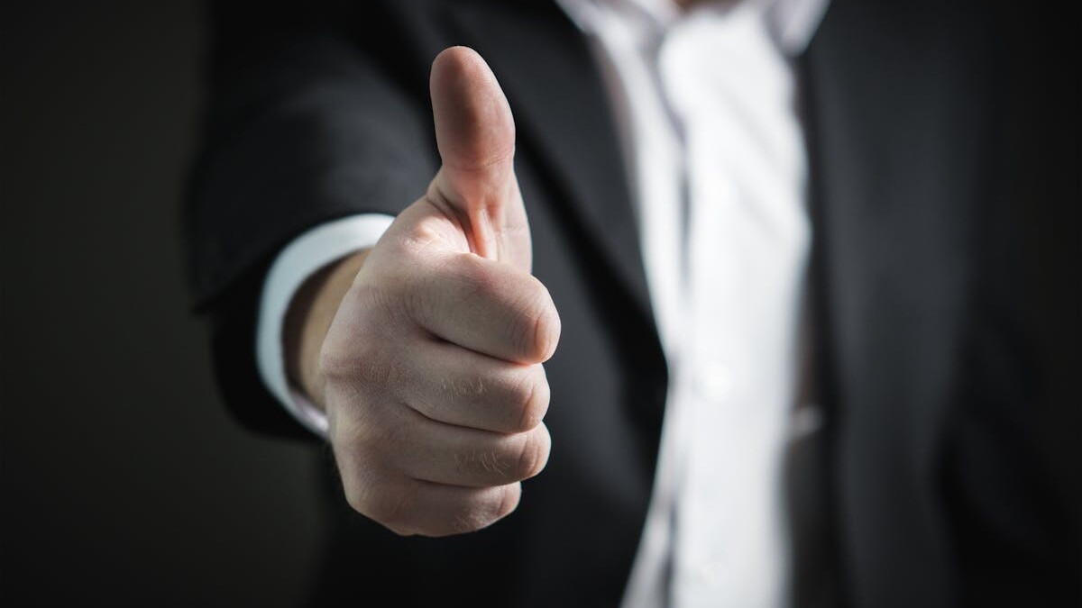 A close-up of a man's thumbs up gesture, symbolizing success and agreement.