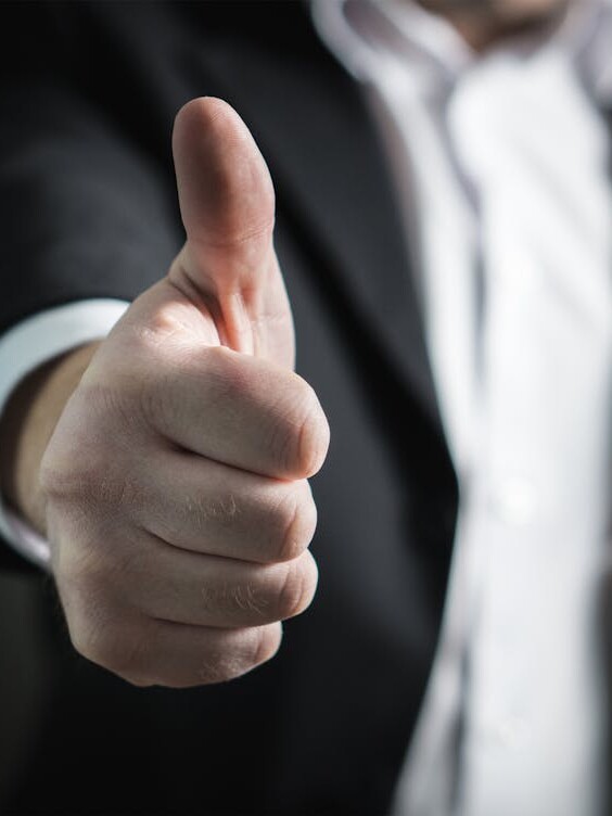 A close-up of a man's thumbs up gesture, symbolizing success and agreement.