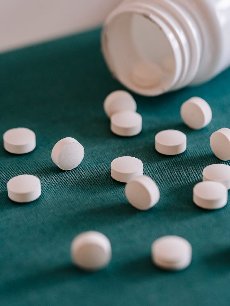 Closeup of spilled similar white round pills placed near plastic container on green surface