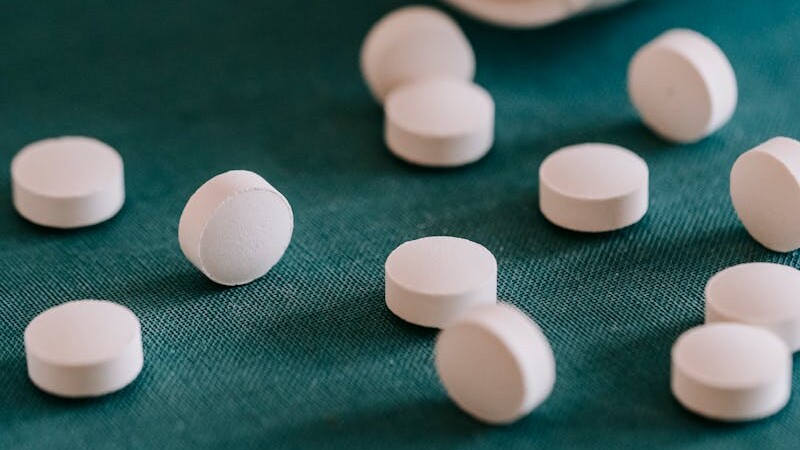 Closeup of spilled similar white round pills placed near plastic container on green surface