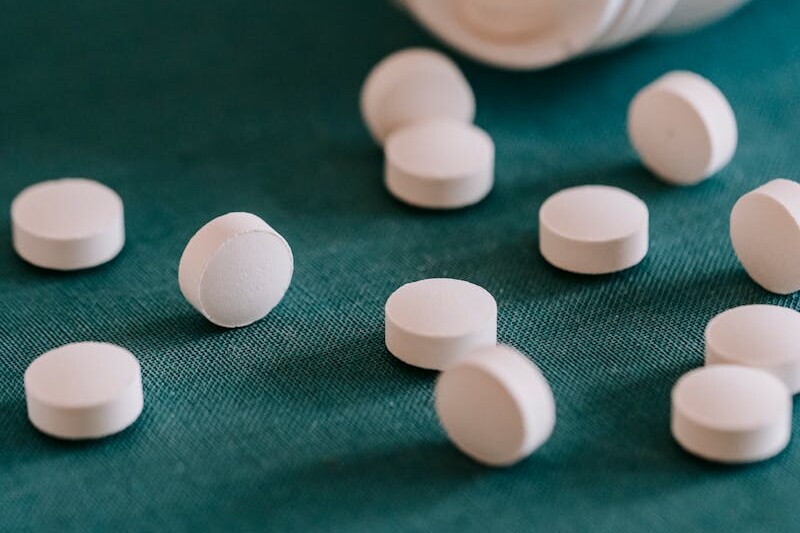 Closeup of spilled similar white round pills placed near plastic container on green surface