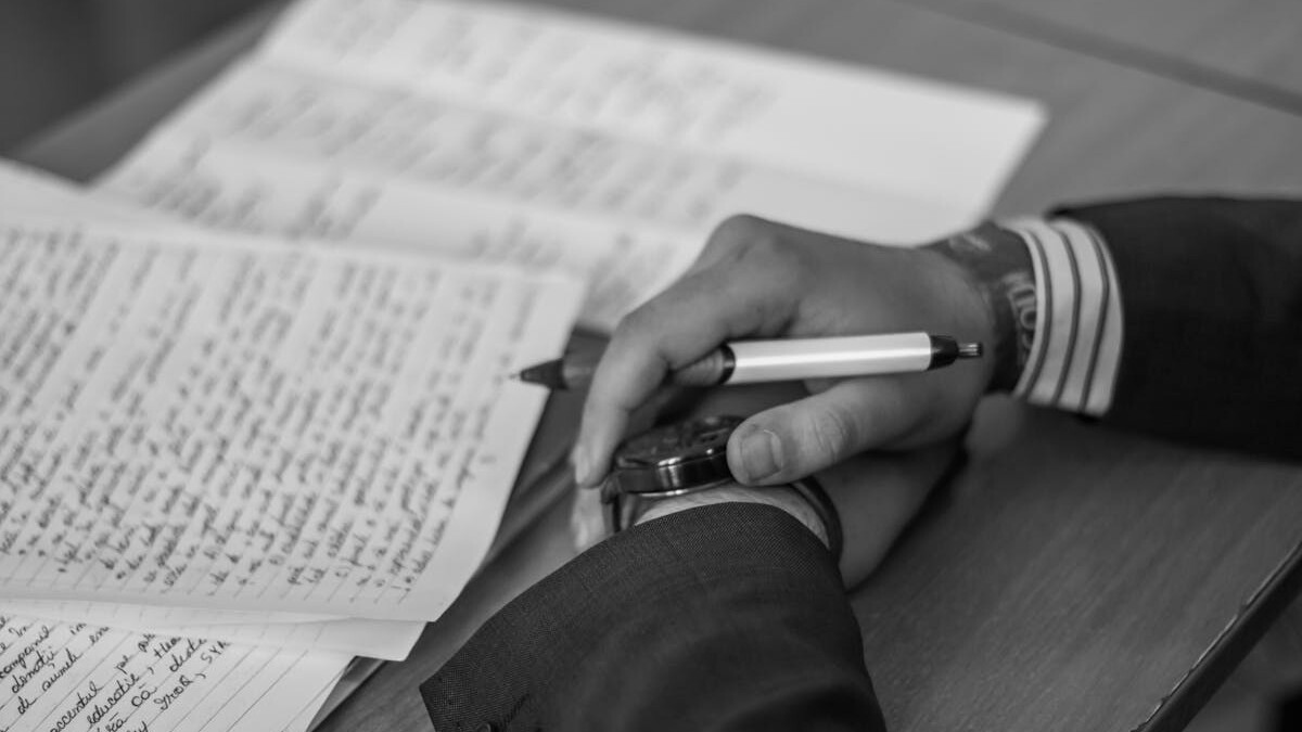 Close-up of a hand holding a pen over pages of writing on a desk.