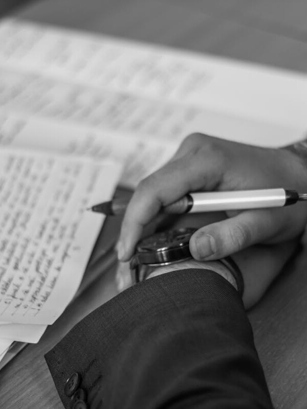 Close-up of a hand holding a pen over pages of writing on a desk.