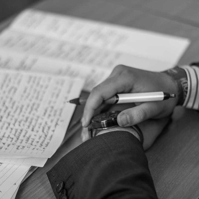 Close-up of a hand holding a pen over pages of writing on a desk.