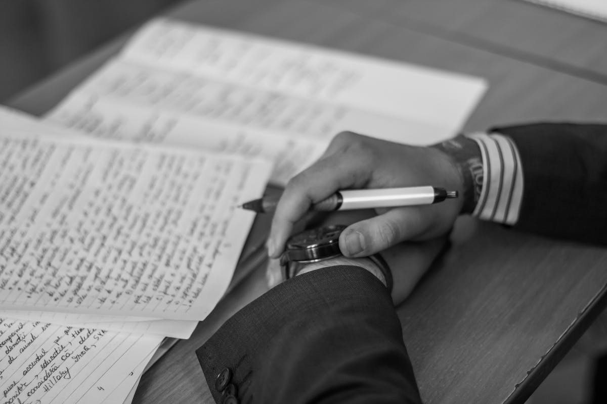 Close-up of a hand holding a pen over pages of writing on a desk.