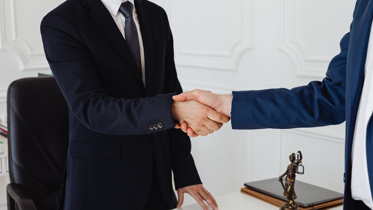 Two men in suits shaking hands in a formal office environment symbolizing an agreement.