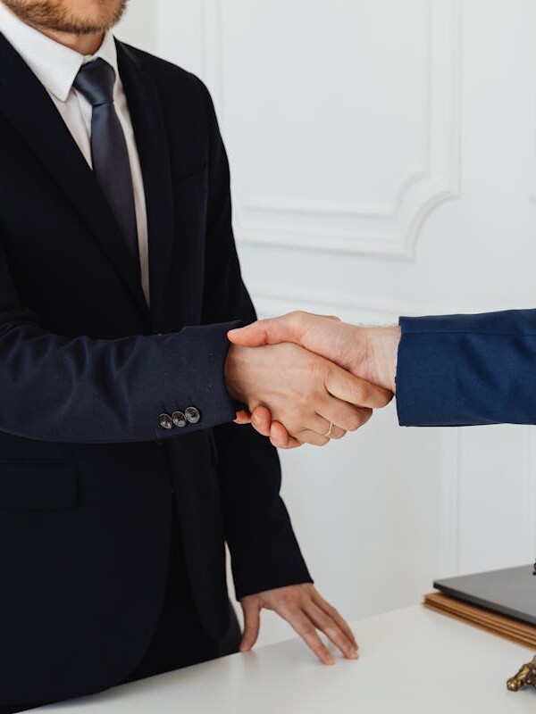 Two men in suits shaking hands in a formal office environment symbolizing an agreement.