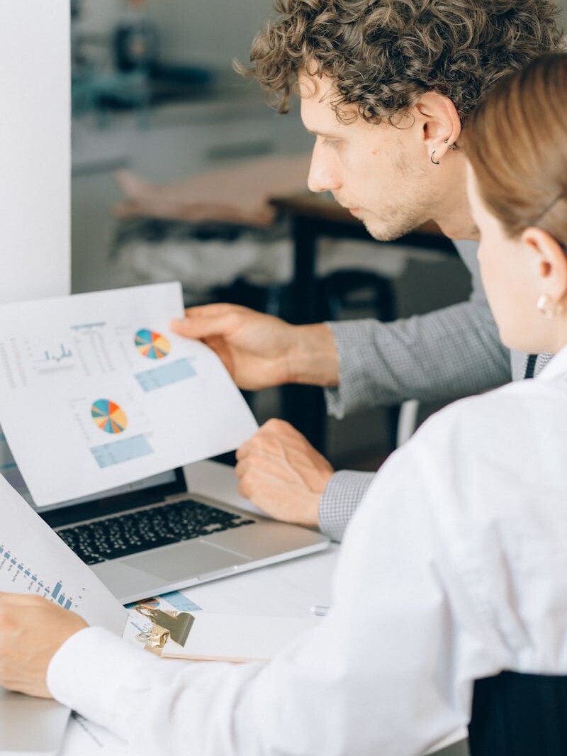 Two business professionals reviewing financial charts and graphs in a modern office setting.