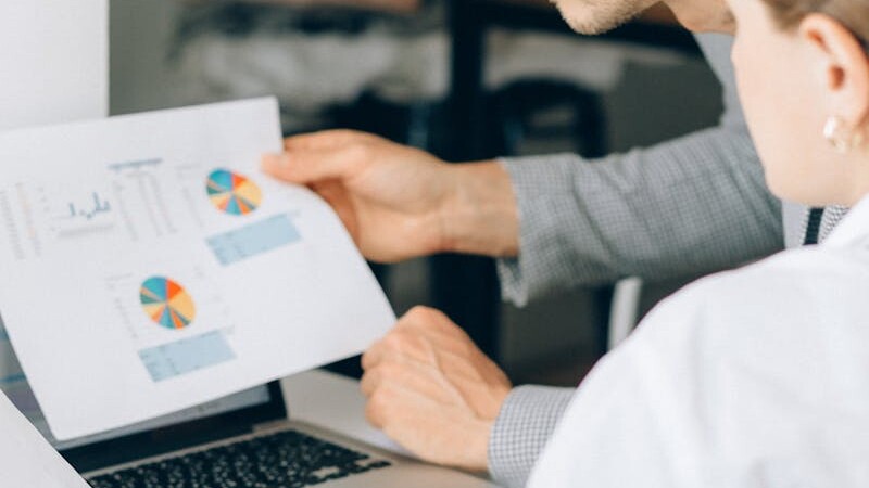 Two business professionals reviewing financial charts and graphs in a modern office setting.