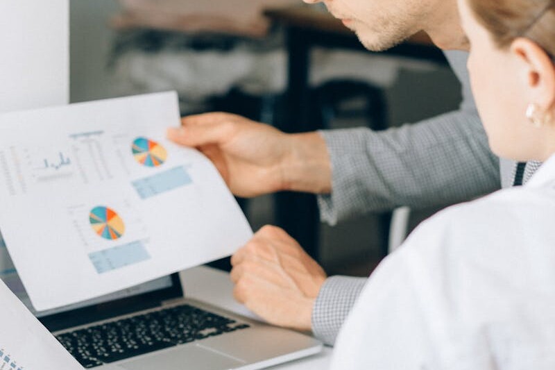 Two business professionals reviewing financial charts and graphs in a modern office setting.