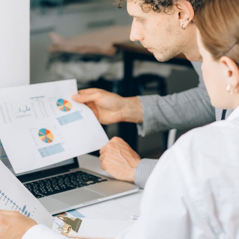 Two business professionals reviewing financial charts and graphs in a modern office setting.