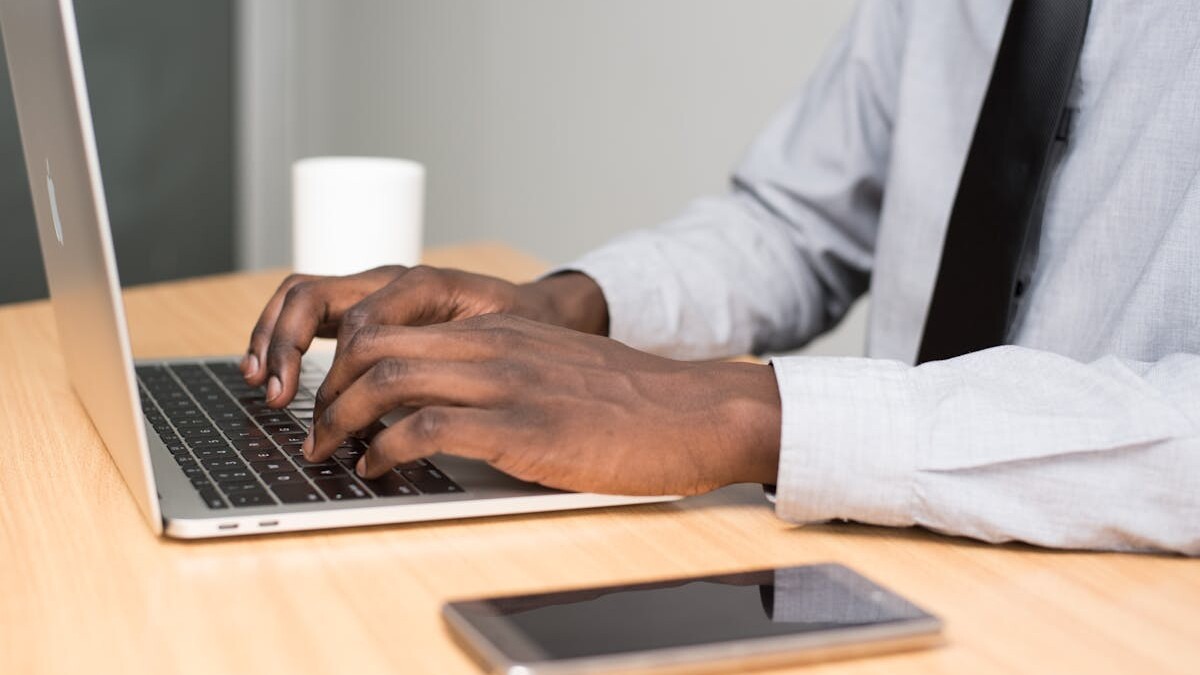 A businessman in office attire working on his laptop at a desk with a smartphone nearby.