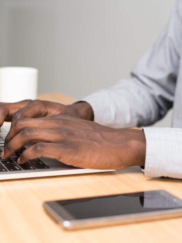 A businessman in office attire working on his laptop at a desk with a smartphone nearby.