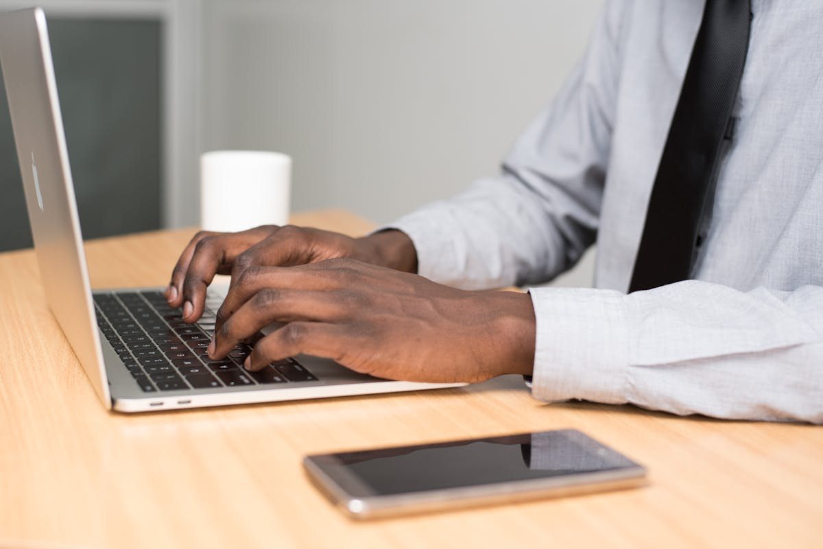 A businessman in office attire working on his laptop at a desk with a smartphone nearby.