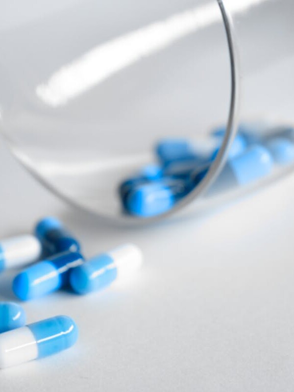 A close-up of blue and white capsules spilling from a glass on a light background.