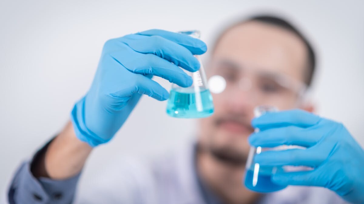 Scientist in a laboratory conducting an experiment, holding blue liquid in flasks with protective gloves.