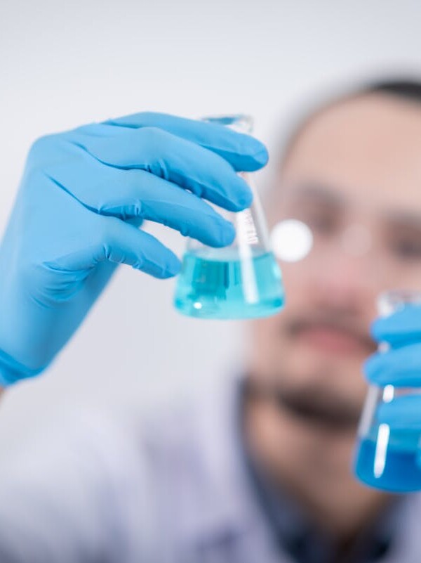 Scientist in a laboratory conducting an experiment, holding blue liquid in flasks with protective gloves.