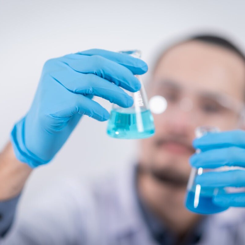 Scientist in a laboratory conducting an experiment, holding blue liquid in flasks with protective gloves.