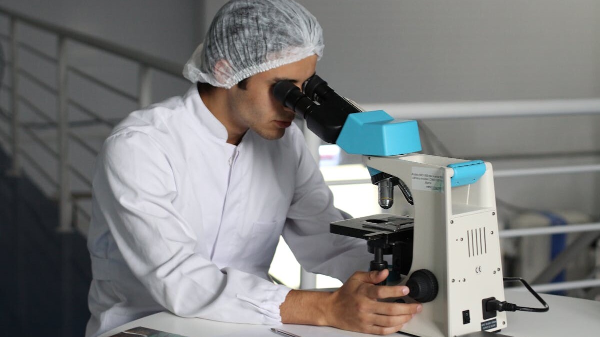 Scientist in a lab coat using a microscope to conduct research, focusing on healthcare improvements.