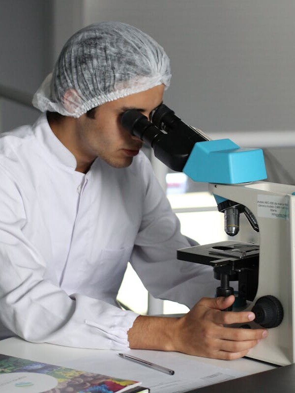 Scientist in a lab coat using a microscope to conduct research, focusing on healthcare improvements.