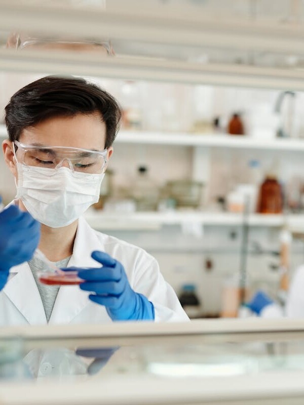 Researcher in a lab coat working on a scientific experiment with a petri dish and protective gear.