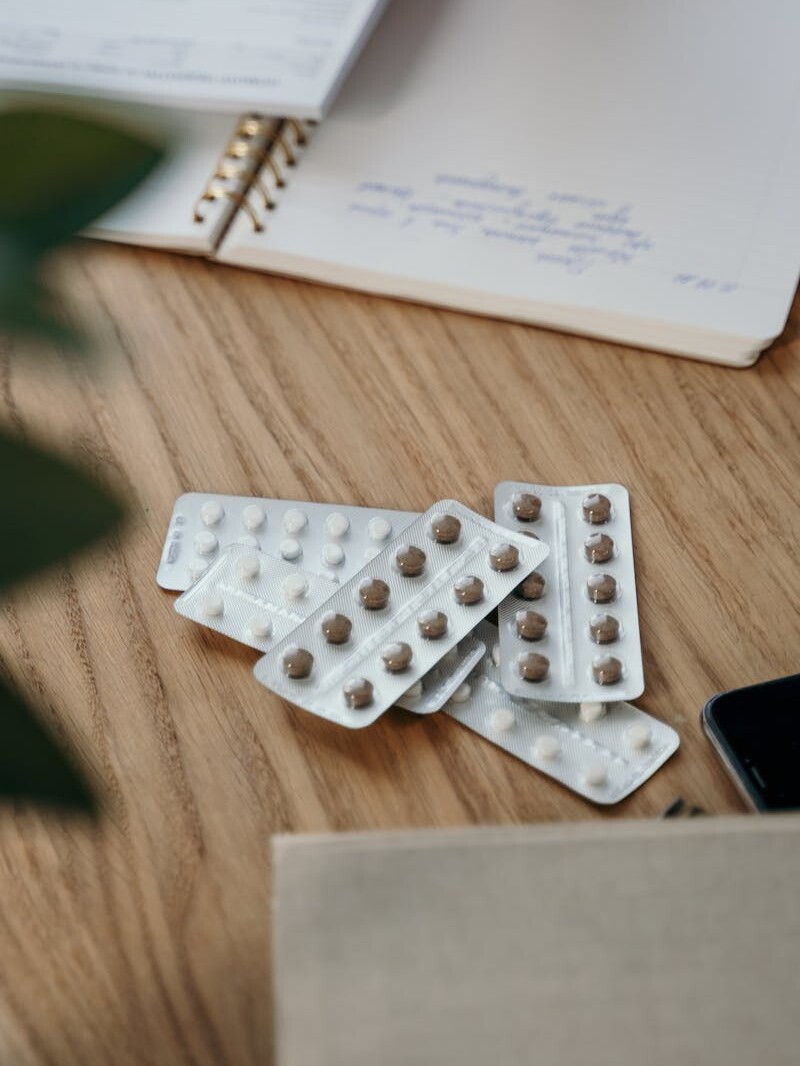 Blister packs with pills on a wooden table alongside an open notebook.