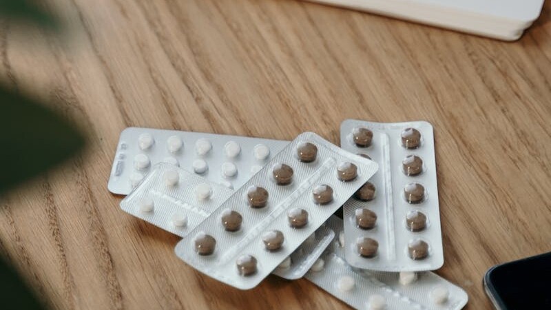 Blister packs with pills on a wooden table alongside an open notebook.