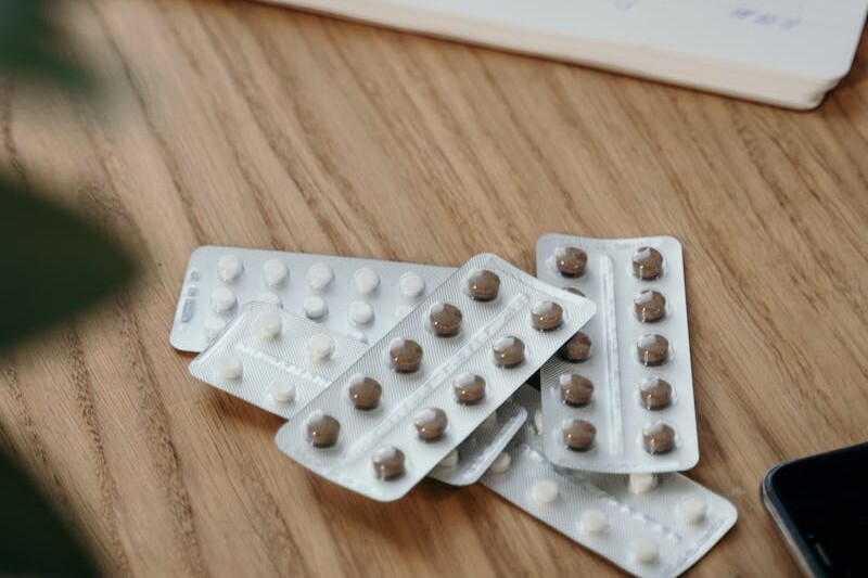 Blister packs with pills on a wooden table alongside an open notebook.