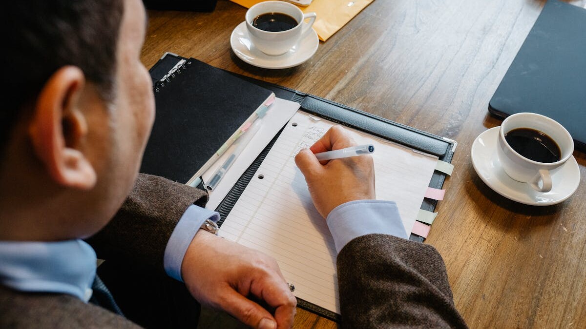 A professional man writes notes at a meeting table with coffee cups.