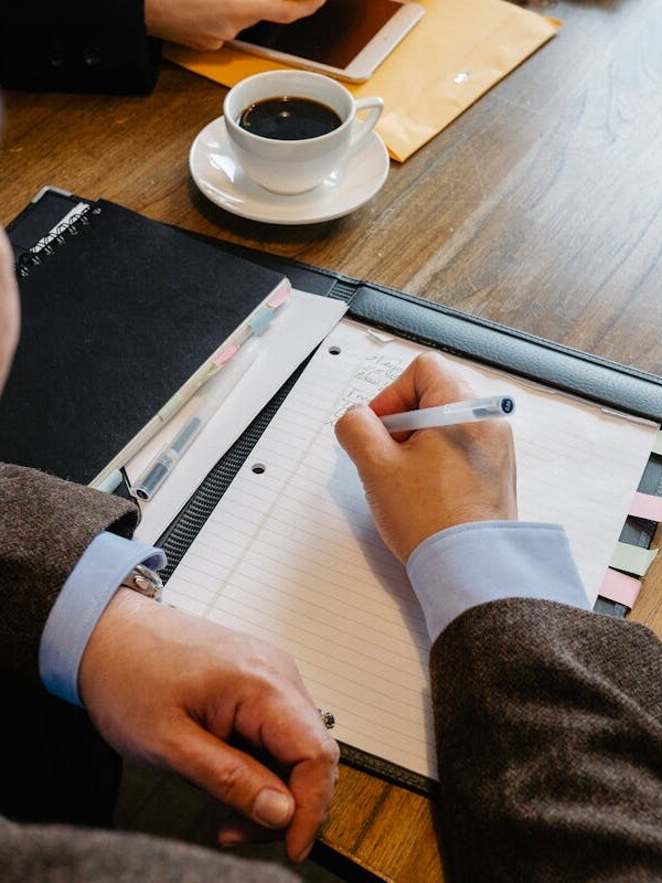 A professional man writes notes at a meeting table with coffee cups.