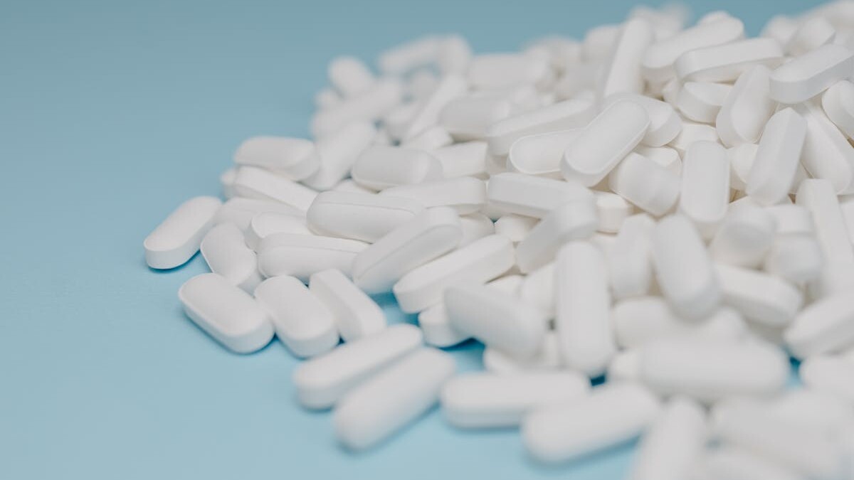 Close-up of white pills scattered on a blue background, focusing on pharmaceuticals.